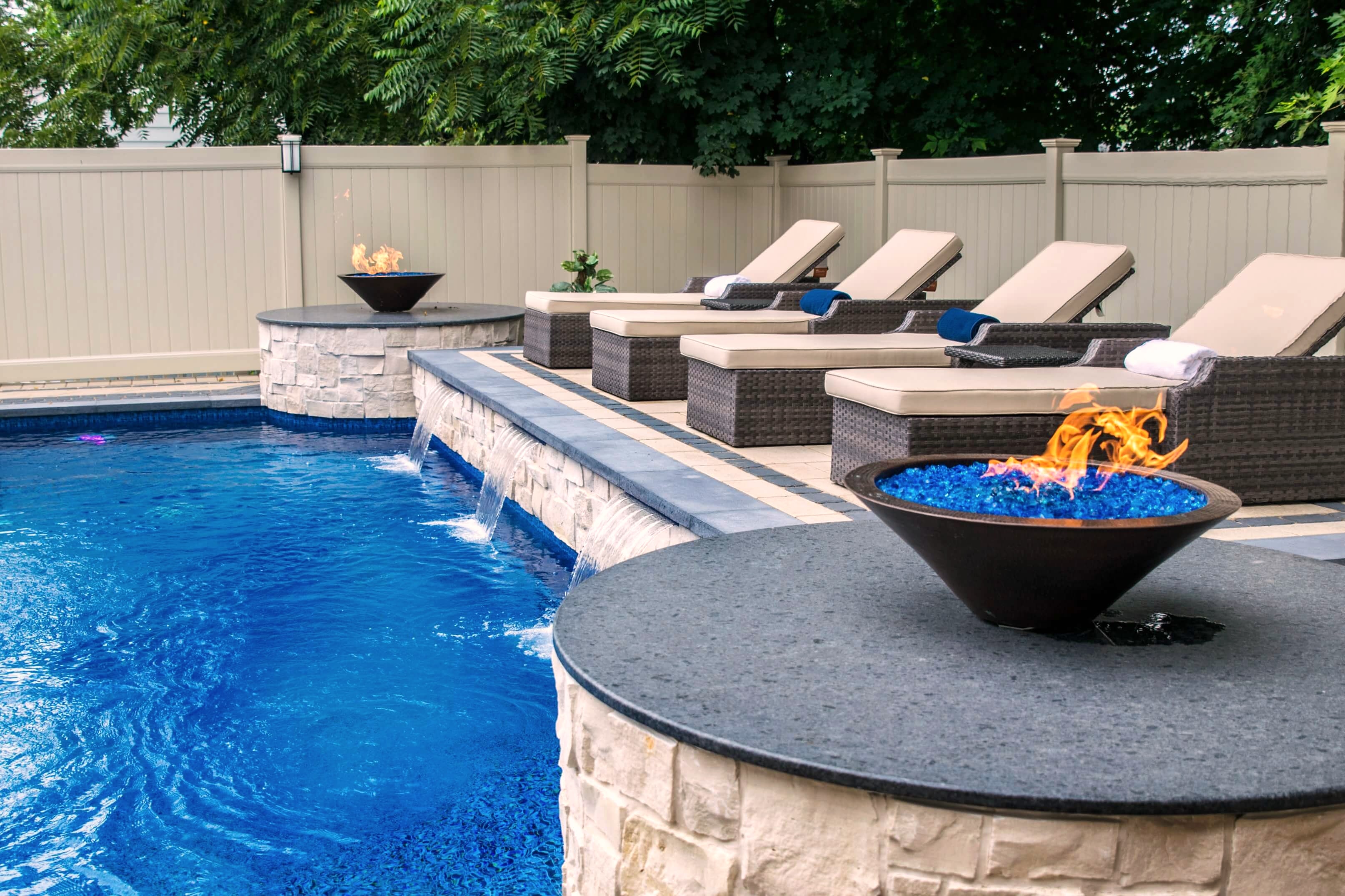 Pool with stone waterfall wall, fire bowls, and lounge chairs