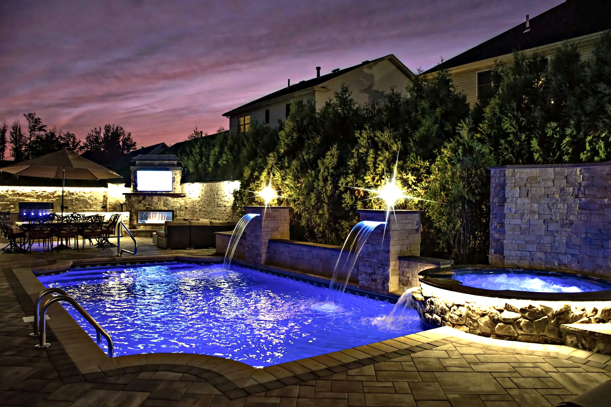 Backyard pool at dusk with lit waterfalls, spa and outdoor fireplace